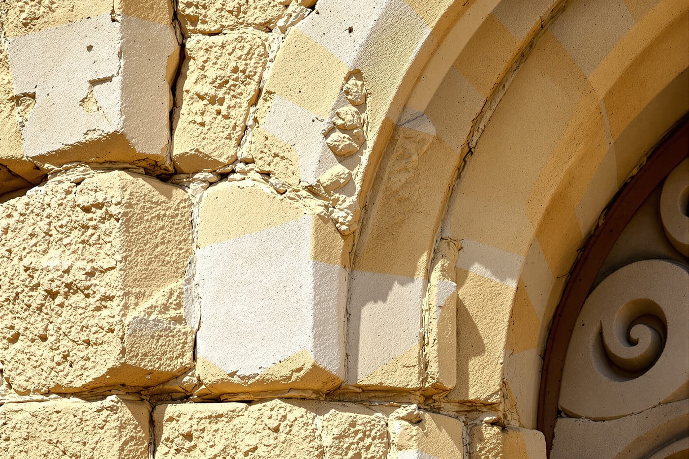 Raking light across weathered medieval limestone ashlar, a pointed arch and a carved acanthus capital